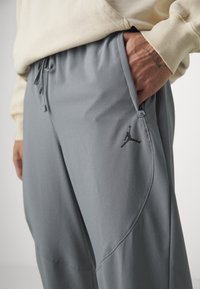 Grå træningsbukser lavet af letvægtsstof, med en sidelomme, snor i taljen og et sort Jumpman-logo på låret.