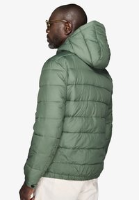 Polstret grøn jakke med hætte, med vandret quiltning, en glat tekstur og knapdetaljer ved manchetterne. Letvægts og afslappet design.