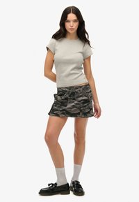 Camiseta ajustada gris de manga corta combinada con una falda de mezclilla con patrón de camuflaje en negro y gris, complementada con calcetines grises y mocasines negros.