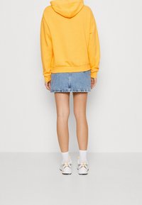 Gul huvtröja med känguruficka, parat med en denim mini kjol. Vita sneakers med gula accenter och synliga ankelstrumpor.