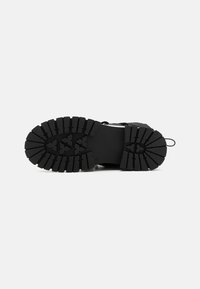 Semelle de chaussure extérieure noire avec un motif de sculpture rugueux, en caoutchouc, conçue pour l'adhérence et la durabilité, avec un talon renforcé.