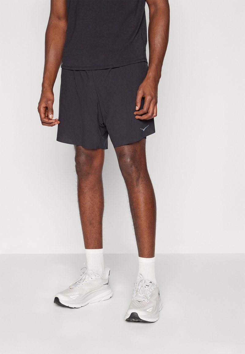 Pantalones cortos deportivos negros de corte ajustado, con un sutil logotipo en la pierna izquierda. Combinados con zapatillas deportivas blancas y calcetines blancos de caña corta.