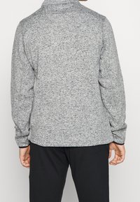 Maglione grigio a maniche lunghe con un colletto alto. Presenta un sottile motivo maculato e una vestibilità ampia, abbinato a pantaloni neri.