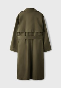 Long trench-coat vert olive avec ceinture et rabat pare-tempête dans le dos, vu de dos sur un fond uni.