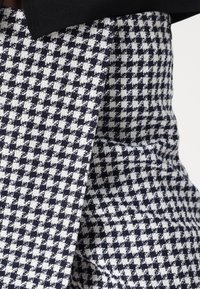 Tessuto a scacchi blu navy e bianco con una trama strutturata, dotato di un colletto nero. La vista ravvicinata mette in evidenza il motivo e i dettagli del materiale.