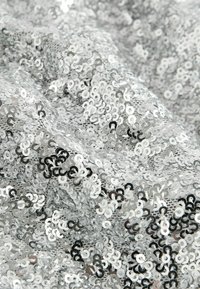 Silberner Paillettestoff mit einer Mischung aus glänzenden, runden Pailletten, die dicht in einer wellenförmigen Struktur angeordnet sind und das Licht aus verschiedenen Blickwinkeln reflektieren.