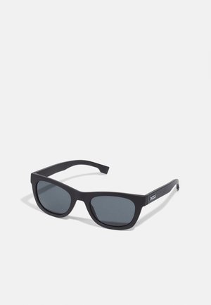 Occhiali da sole rettangolari neri con lenti scure. Realizzati in plastica opaca, presentano una montatura dritta e aste con il marchio "BOSS" sul lato.