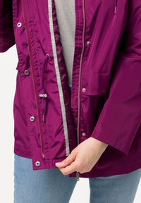 Lila vattentät jacka med dragkedja och tryckknappsstängning, justerbar dragsko i midjan samt tryckknappsfickor framtill.