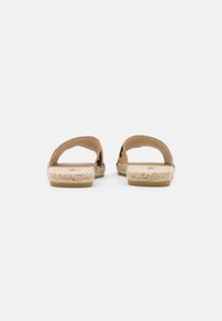 Tan slip-on sandals with a woven straw sole, open heel and toe design, and smooth leather-like upper. No visible patterns or accents.