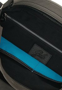 Interno di una borsa in pelle grigia con fodera nera, tasca in tessuto blu, scomparto con zipper e etichetta nera a texture.