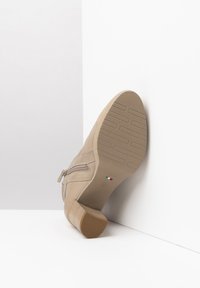 Stivale beige alla caviglia con tomaia in pelle liscia, cerniera laterale e tacco basso a blocco. Suola testurizzata per una migliore aderenza, con un discreto dettaglio della bandiera italiana.