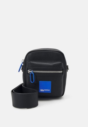 Schwarze Leder-Crossbody-Tasche mit silbernem Reißverschluss, blauen Akzentdetails, einer Fronttasche und verstellbarem Tragegurt. Die Maße sind ca. 20x20 cm.