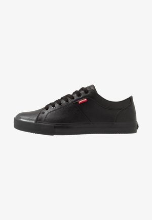 Basket basse noire avec lacets noirs, semelle en caoutchouc, et petite étiquette rouge avec le logo Levi's sur le côté.