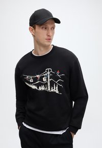 Μαύρο φούτερ με λευκό γραφικό τοπίου και τελεφερίκ. Διαθέτει ριμπ μανσέτες και λαιμόκοψη crew. Φοριέται με μαύρο καπέλο.