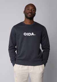 Navyblaues Sweatshirt mit langen Ärmeln, das in der Mitte mit dem weißen Aufdruck "OIDA." versehen ist. Hergestellt aus einem weichen, glatten Material.