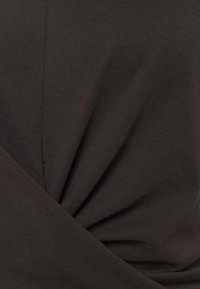 Tela negra con una textura suave presenta un diseño retorcido en el centro, creando suaves pliegues y caídas delicadas. Tomada desde un ángulo.