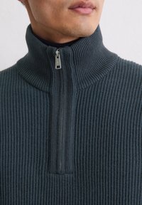 Donkergrijze geribde pullover met hoge kraag en halve rits, voorzien van een gestructureerde stof en subtiele stikdetails.