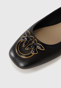 Black leather flat shoe with square toe featuring two black and gold bird-shaped decorative ornaments on top.