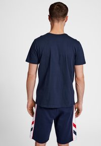 Mörkblå kortärmad T-shirt med rund halsringning, i kombination med mörkblå shorts med röda och vita snedstreck på sidorna.