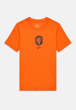 Klar orange Nike t-shirt med korte ærmer, med et sort løveemblem og Nike swoosh-logo centreret på brystet.