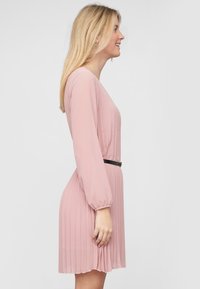 Abito plissettato rosa chiaro con maniche lunghe, scollo a V e una cintura nera slim in vita. Texture liscia, design fino al ginocchio.