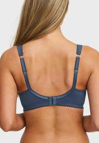 Vrouw met lang blond haar, die een blauwe beha draagt, gezien van achteren met verstelbare banden en haak-en-oogsluiting.