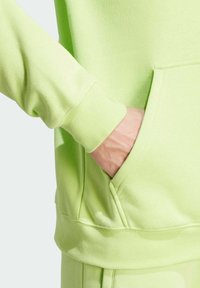 Limegrön hoodie med mjuk textur, prydd med en känguruficka och ribbade mudd. Designen är enkel och avslappnad.