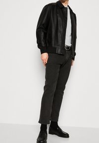 Musta nahkainen bomber-takki, jossa on resorit hihansuiden kohdalla, pyöreäkauluksinen t-paita, tummanharmaat farkut ja mustat loaferit. Yksinkertainen, istuva muotoilu ja sileä pinta.