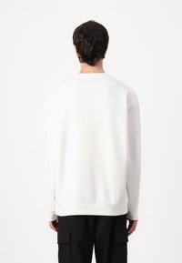 Sudadera blanca de manga larga, con cuello redondo y puños de canalé, combinada con pantalones cargo negros. Textura suave, diseño minimalista.