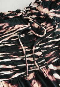 Crna i ružičasta tkanina s tie-dye uzorkom i nabranom teksturom. Ima vezicu i slojeviti dizajn, ističući mekan i lepršav izgled.