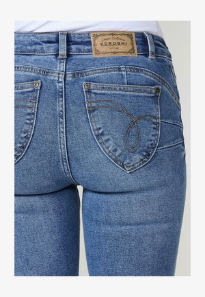 Kék dzsungel farmernadrág, amely fitted dizájnnal, látható varrással és két hátsó zsebbel rendelkezik. A derékpánton egy márkázott bőrcímke található.