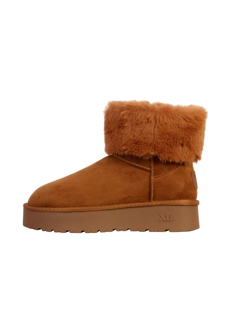 Bottes chelsea en suédine marron avec un large revers en fausse fourrure beige, semelle en caoutchouc et couture sur les côtés. Logo Xti en relief sur le talon.