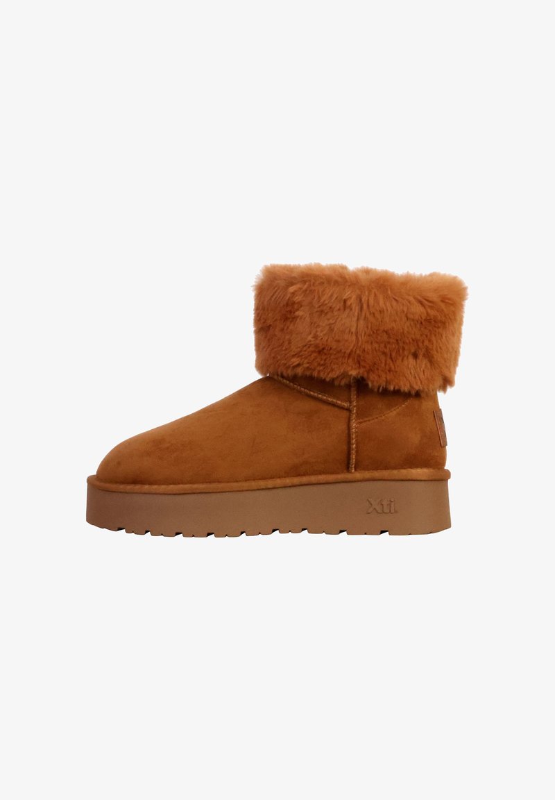 Stivaletti alla caviglia in suede marrone con un soffice risvolto in peli sintetici color cammello, suola in gomma e cuciture sulla cucitura laterale. Logo Xti impresso sul tallone.