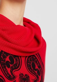 Rode gebreide trui met een brede, gedrapeerde col en een zwart grafisch ontwerp met textuurring accenten. Gladde stof met zichtbare ribbels.