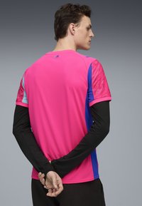 Ljusrosa träningströja med korta ärmar i rosa och blått, med svarta långa ärmar under. Texturerad tyg på axlarna.