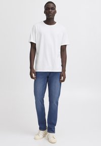 Fehér pamut póló kerek nyakkivágással, kék farmernadrággal és törtfehér tornacipővel párosítva. Egyszerű kialakítás, normál szabás.