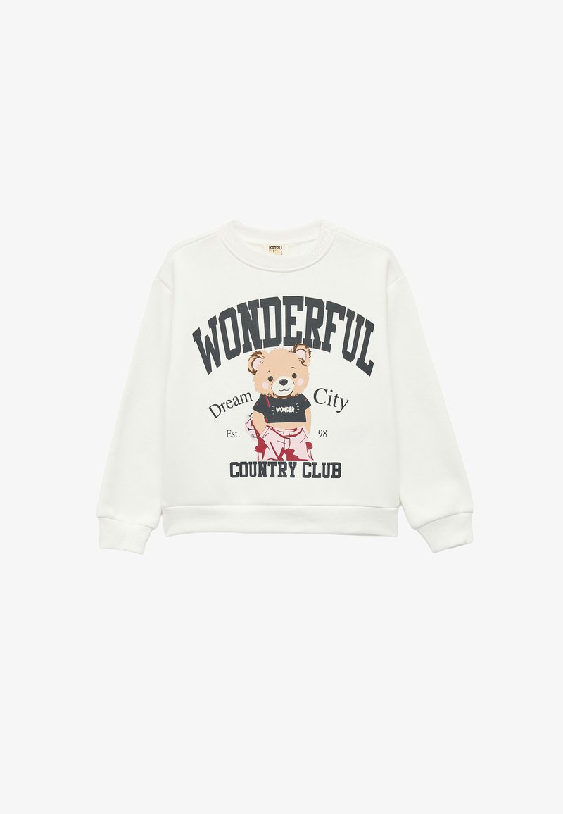 Biała bluza z okrągłym dekoltem, z grafiką niedźwiedzia w czarnej koszulce. Napis głosi „CUDOWNY”, „Miasto Marzeń” i „KLUB KRAJOWY.”