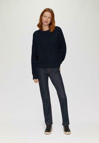 Marineblauwe geribbelde gebreide trui met een relaxte pasvorm, gecombineerd met donkere denim broek en zwarte sneakers met een gestructureerde zool.