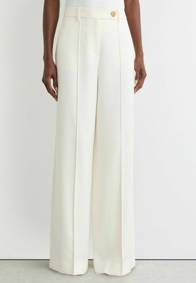 Pantalon à jambes larges en tissu crème, avec taille haute, plis à l'avant et fermeture par un seul bouton. Texture lisse avec une coupe ajustée.