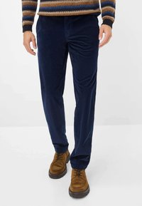 Marineblaue Cordhosen mit strukturierter Oberfläche, geradem Bein und seitlichen Taschen, kombiniert mit braunen Wildleder Schnürstiefeln.