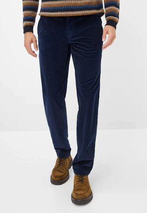 Marineblauwe ribfluwelen broek met een gestructureerde afwerking, rechtvallend ontwerp en zijzakken, gecombineerd met bruine suède veterschoenen.