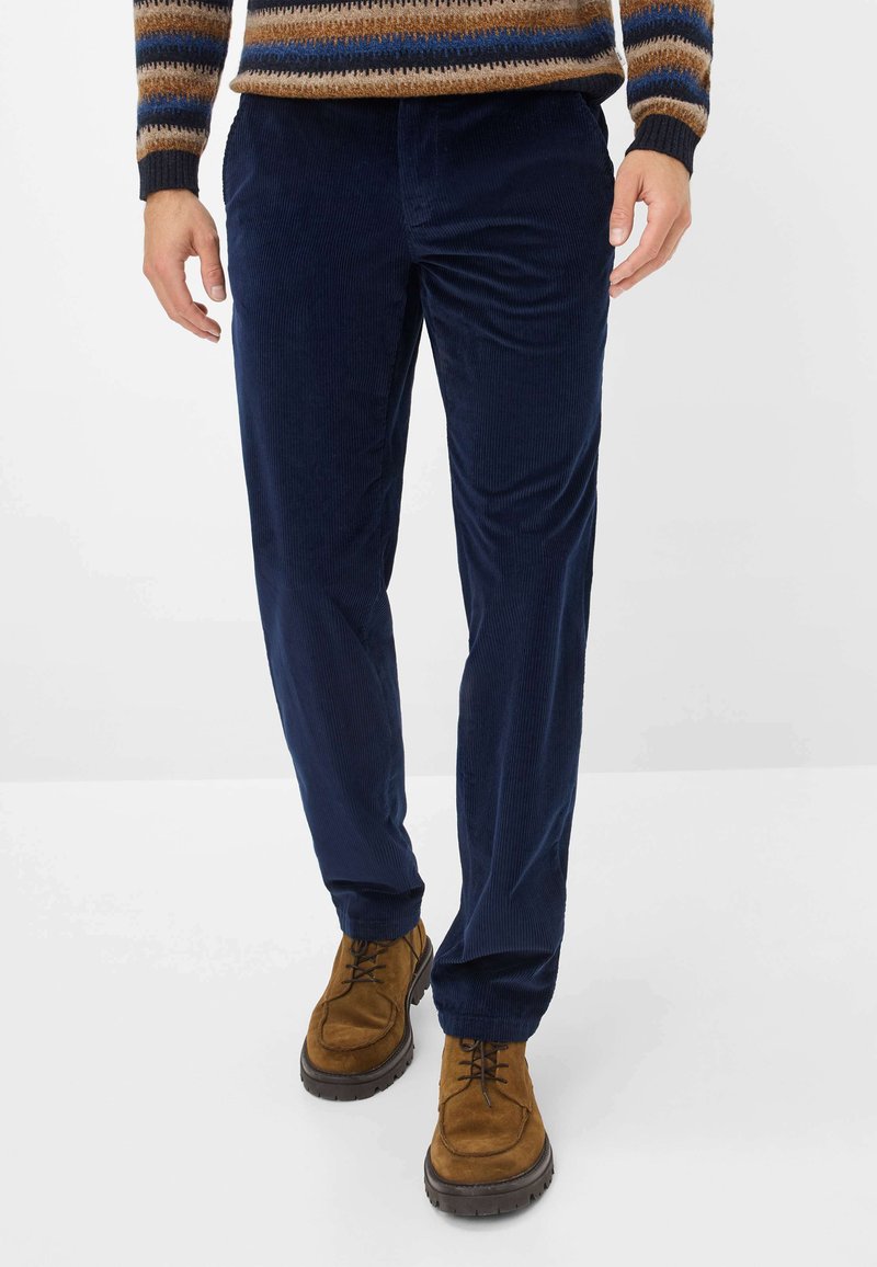 Marineblaue Cordhosen mit strukturierter Oberfläche, geradem Bein und seitlichen Taschen, kombiniert mit braunen Wildleder Schnürstiefeln.