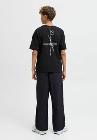 Černé tričko s bílým grafickým textem na zádech, spárované s tmavými, volnými kalhotami a bílými teniskami.