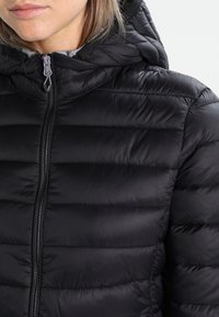 Zwarte gewatteerde jas met een capuchon, voorzien van gequiltete delen, een volledige ritssluiting en een zachte binnenvoering. Textuur, lichtgewicht materiaal.