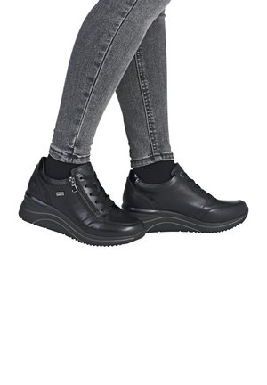 Baskets en cuir noir avec surface texturée, fermeture par lacets et zip, semelle compensée rembourrée et semelle extérieure en caoutchouc durable. Jeans skinny gris visibles.