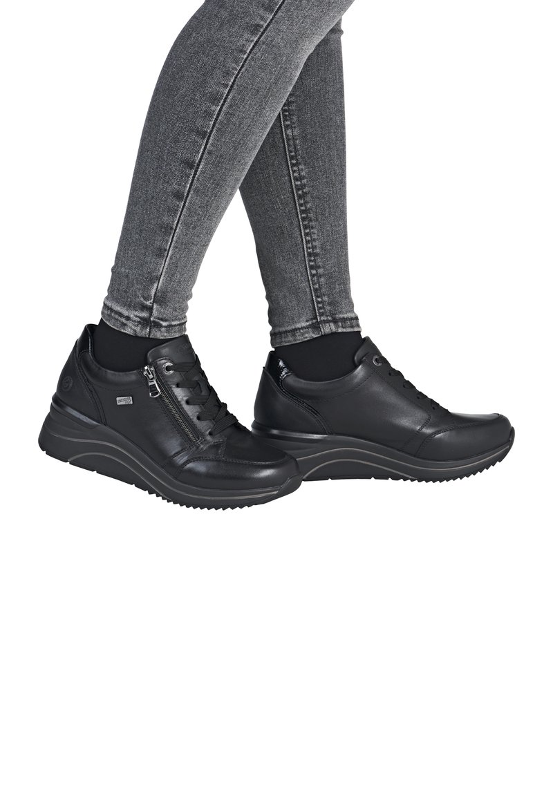 Baskets en cuir noir avec surface texturée, fermeture par lacets et zip, semelle compensée rembourrée et semelle extérieure en caoutchouc durable. Jeans skinny gris visibles.