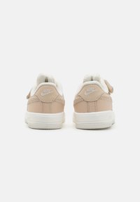 Beige Nike-sneakers med vita detaljer, läderöverdel, sydda detaljer och rem med krok och ögla. Texturerad sula för grepp.