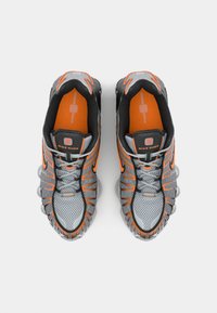 Nike Shox sneakers in gray with orange accents. Mesh upper, padded collar, and rubber sole with spring-like cushioning elements.