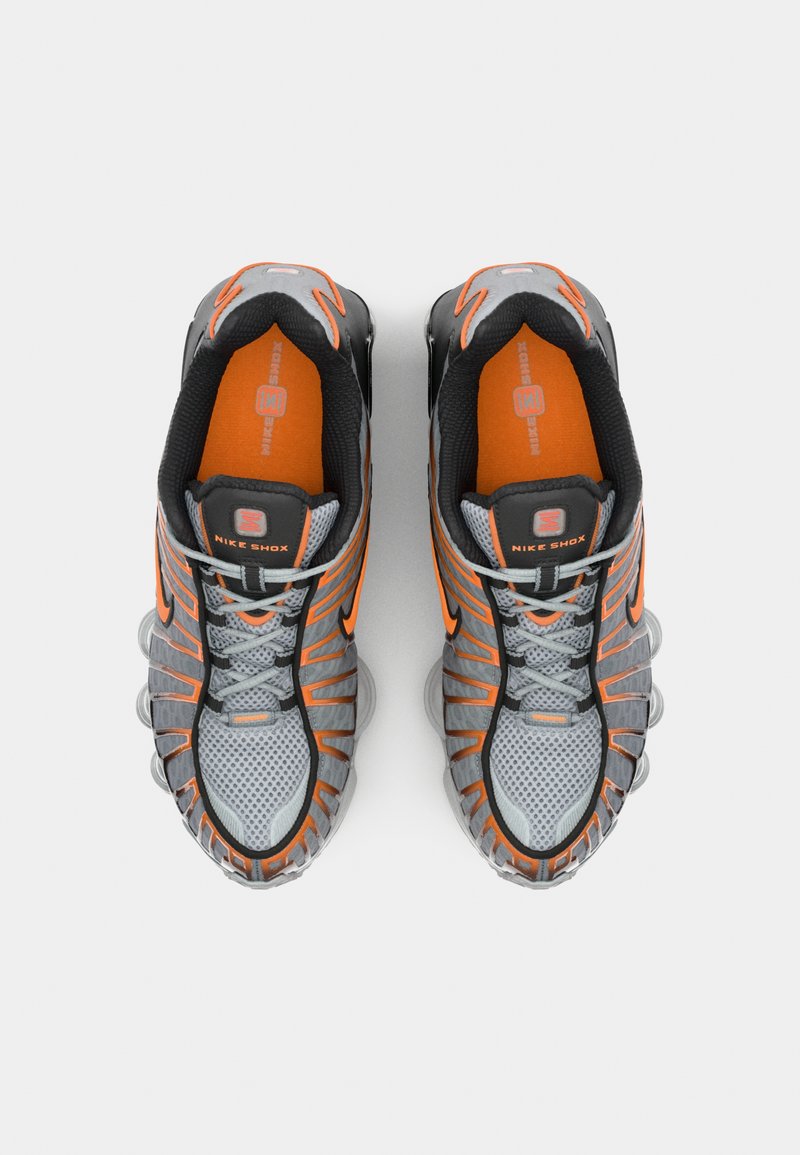 Baskets Nike Shox grises avec des accents orange. Tige en maillage, col rembourré et semelle en caoutchouc avec des éléments d'amortissement semblables à des ressorts.