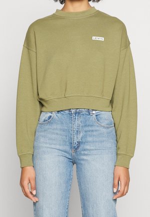 Osoba ubrana w jasnozieloną skróconą bluzę Levi's i jasnoniebieskie jeansy z wysokim stanem, stojąca na jednolitym tle.